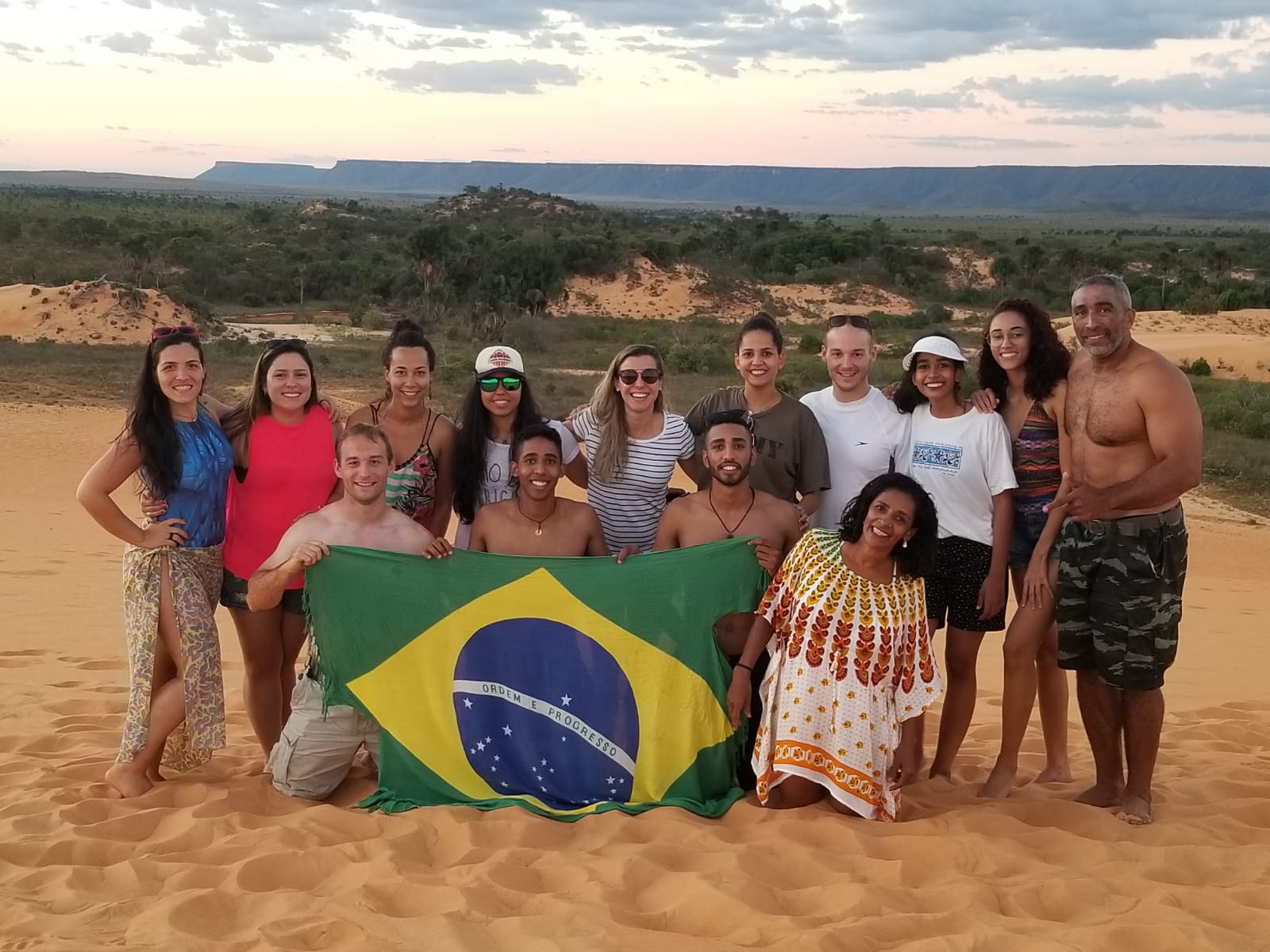 Family and new friends holding a Brazilian flag on the sand dunes of Jalapão